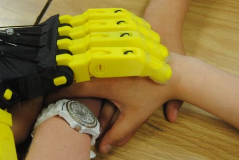  A mechanical hand created by students is placed on top of human hands as a gesture of teamwork.